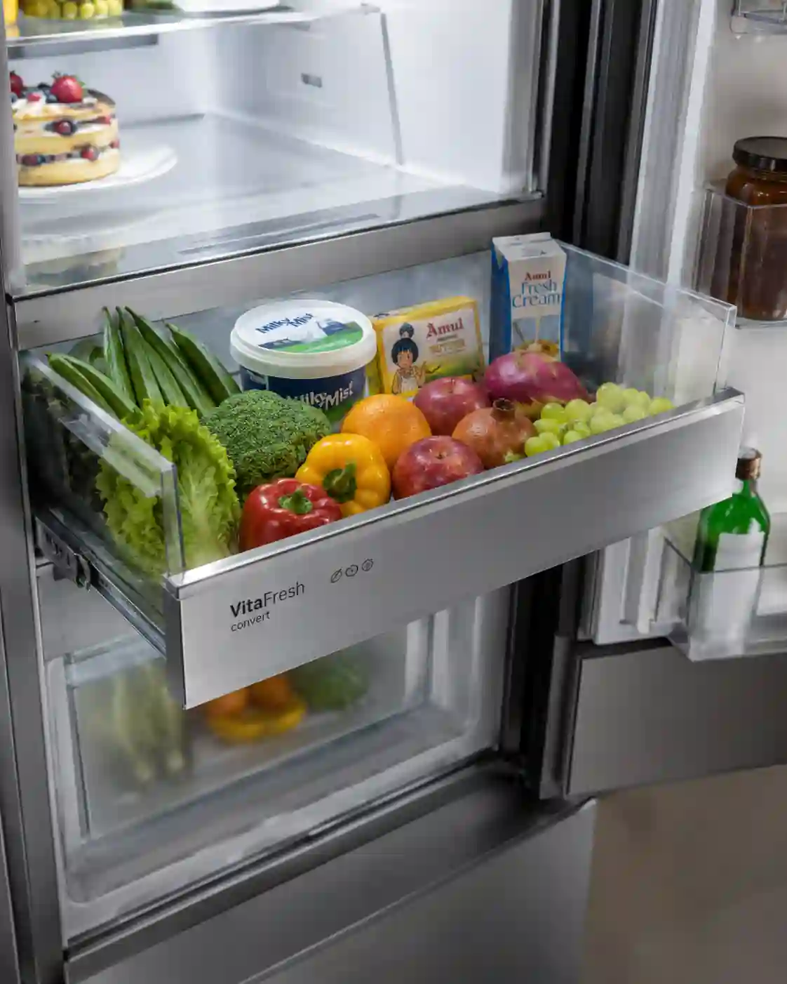 Bosch 303L refrigerator middle convertible drawer filled with fresh vegetables, fruits, and dairy products in bright hygienic interior.