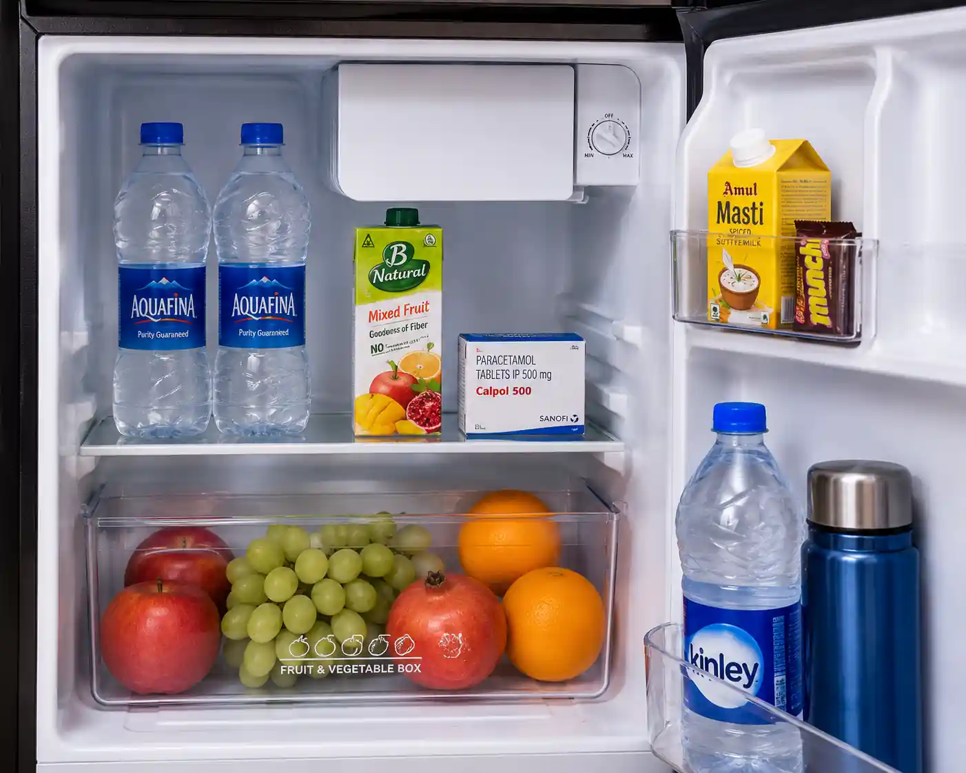 Inside view of Rockwell mini fridge with water bottles, juice carton, medicine box, and fresh fruits